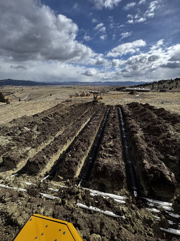 Septic system installation with exposed tank and drain field before backfilling in Montana